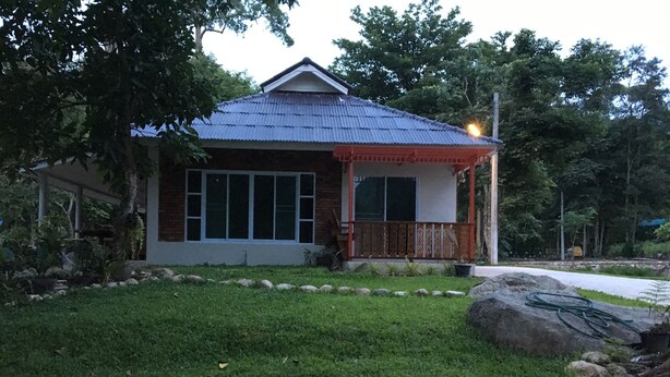 A house with a blue roof, a porch with a railing, and a lawn with rocks and plants. - Lundaresort & Orchid (Suan Phueng)