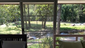 Una habitación con dos camas, un ventanal grande y vistas a un jardín con árboles y un arroyo.