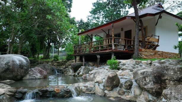 Una cabaña rústica con terraza de madera y una pequeña cascada.