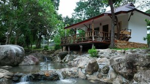 A rustic cabin with a wooden deck and a small waterfall. - Lundaresort & Orchid (Suan Phueng)