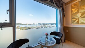 Un balcón con mesa y sillas de vidrio, un jarrón con flores, y vista a un puerto deportivo y paisaje urbano.