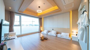 Habitación de hotel moderna con un ventanal grande, suelo de madera, cama con ropa blanca y una bata colgada en la pared.