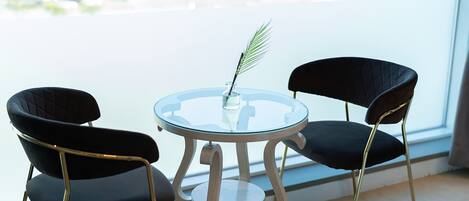 Une pièce moderne avec une table ronde en verre, deux chaises noires à revêtement en tissu et un vase contenant une seule plante verte.