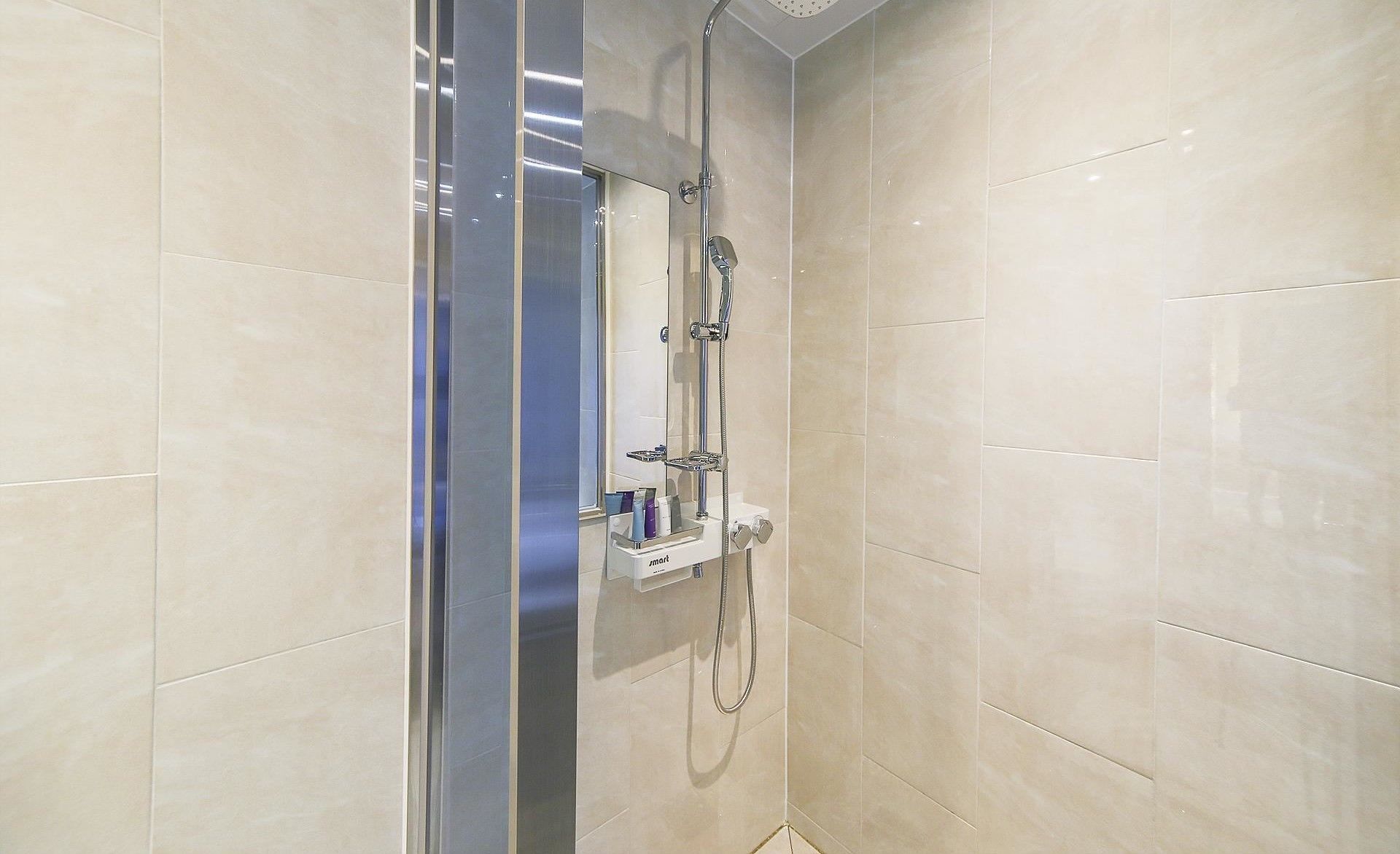 A modern shower with a glass door, a handheld showerhead, and a wall-mounted control panel.