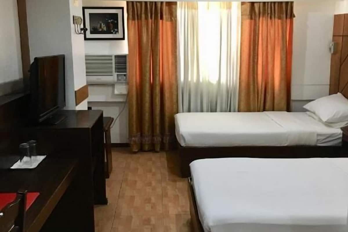 A hotel room with two beds, a desk, a television, and a window with curtains.