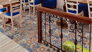 Un coin repas agrémenté de carreaux de sol à motifs, de chaises en bois avec des coussins bleus et d’un miroir décoratif.
