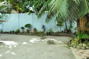 Une cour en béton avec un petit muret en pierre, des plantes en pot et un palmier.