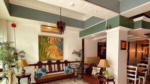 Un hall d’entrée spacieux avec un plafond haut, une grande peinture et un coin salon agrémenté de meubles en bois et de plantes en pot.