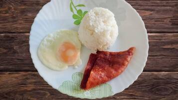 A plate with white rice, a fried egg, and a piece of bacon on a wooden table.