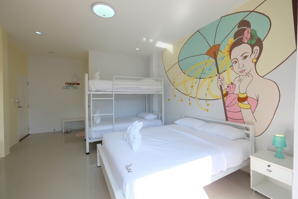 Habitación de hotel con literas, cama individual, un mural en la pared, una mesita de noche con lámpara y una puerta.