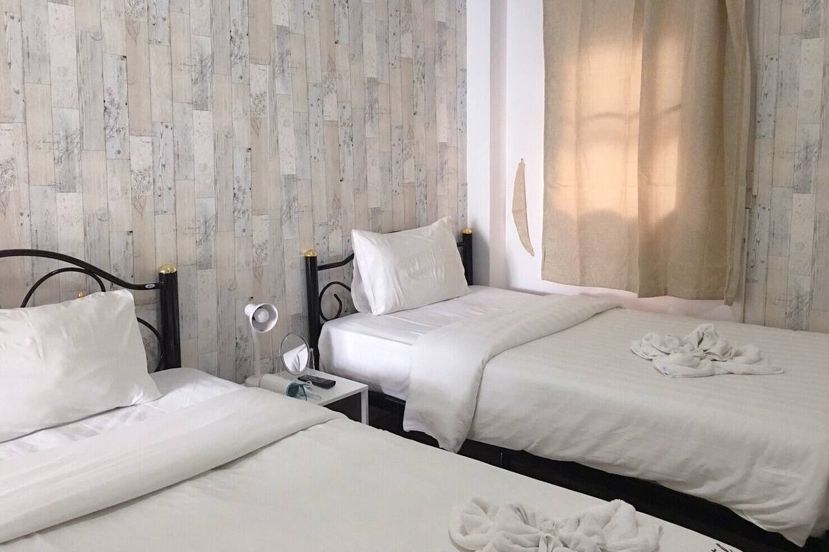 Ein Hotelzimmer mit zwei Betten, einem Nachttisch mit Lampe und einem Fenster mit Vorhängen.