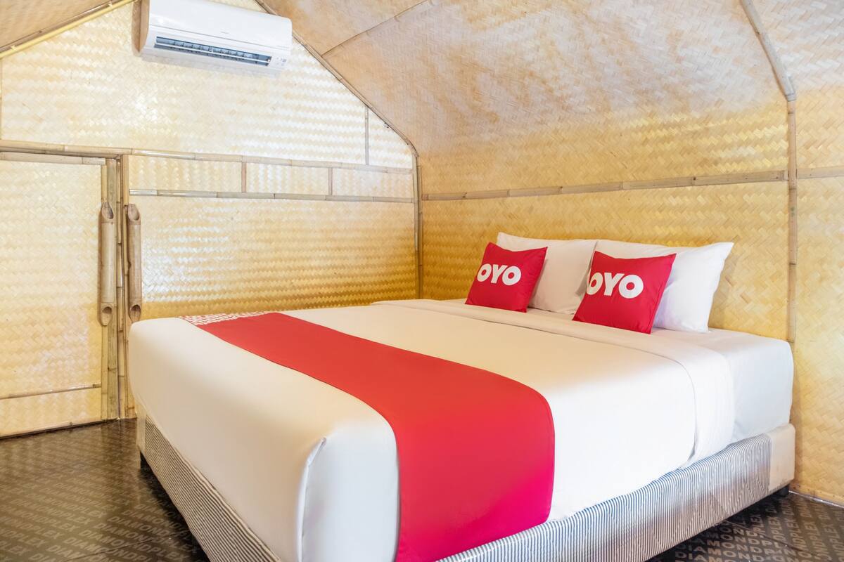 Un lit avec une literie blanche et rouge, deux oreillers rouges ornés du mot « oyo », et une couverture rouge.