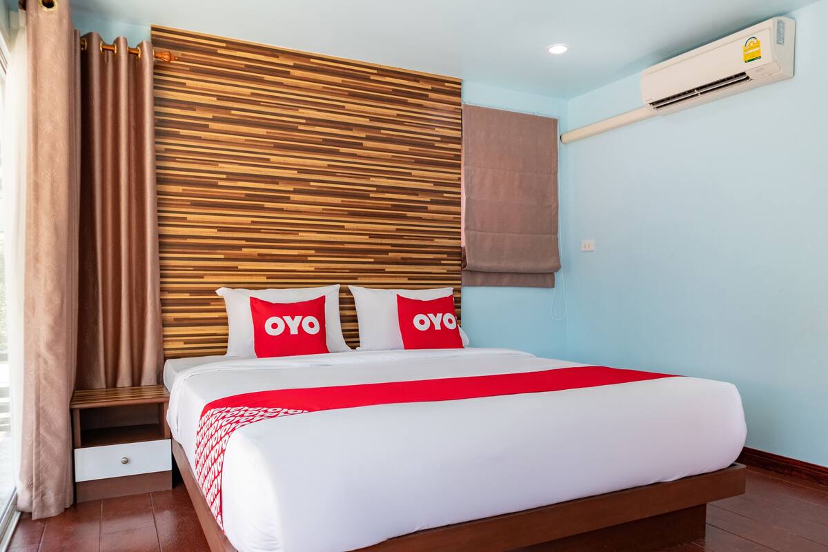 Une chambre d’hôtel avec une tête de lit en bois, un lit avec une literie blanche et rouge, un plaid rouge et un appareil de climatisation fixé au mur.