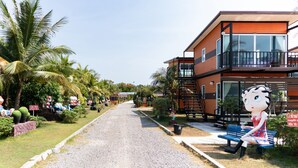 A street with a large statue of a cow, palm trees, and a building with a balcony. - OYO 755 Rattana Resort (Ko Lanta)