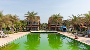A pool area with palm trees, lounge chairs, and a building with balconies. - OYO 755 Rattana Resort (Ko Lanta)