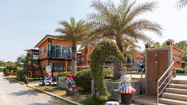 A modern building with a glass facade, palm trees, and a small statue of a character. - OYO 755 Rattana Resort (Ko Lanta)