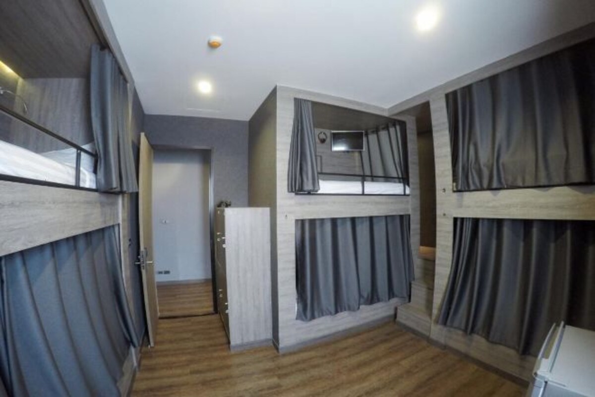 A room with bunk beds, wooden flooring, and grey curtains.