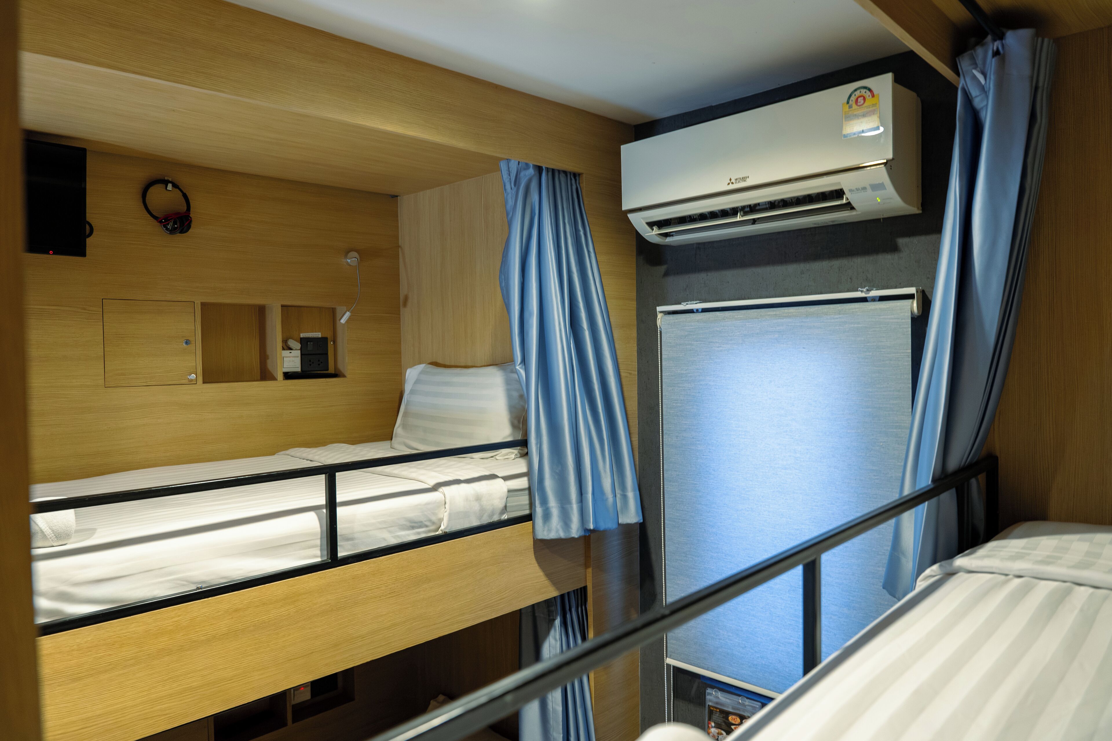 A compact, well-lit room with bunk beds, a small desk, and an air conditioning unit.
