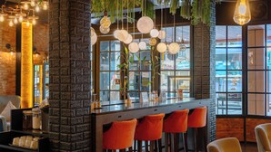 Eine Bar mit Backsteinwand, hängenden Lampen und orangefarbenen Barhocker.