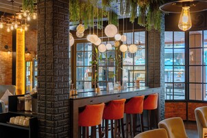 Un área de bar con pared de ladrillo, lámparas colgantes y taburetes naranjas.