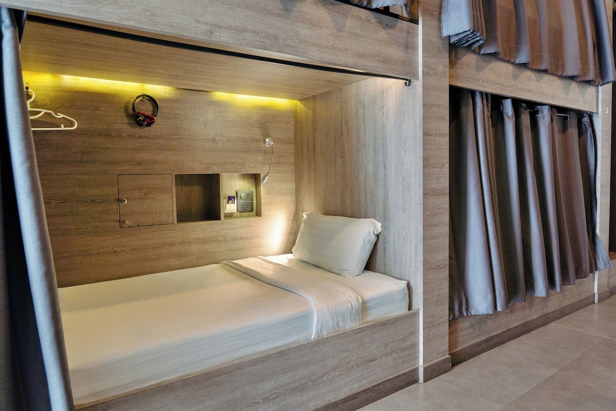 A modern hotel room with a built-in bed, wooden paneling, a small bedside table, and a wall-mounted mirror.
