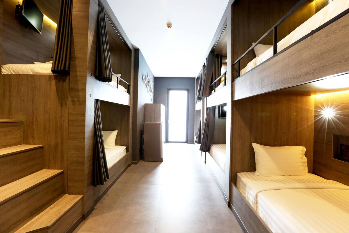 A narrow hallway with bunk beds on either side, a door at the end, and a refrigerator against the wall.