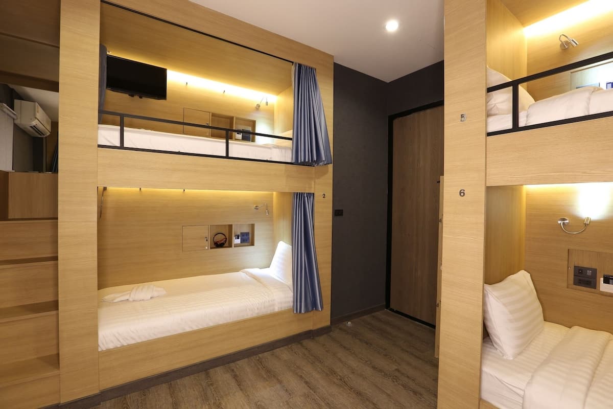 A hotel room with bunk beds, wooden walls, a TV, and a small shelf with a clock.