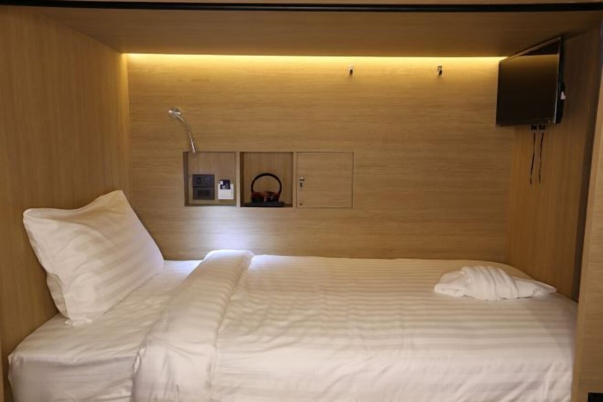 A hotel room with a bed, a television mounted on the wall, and a small shelf with a basket.