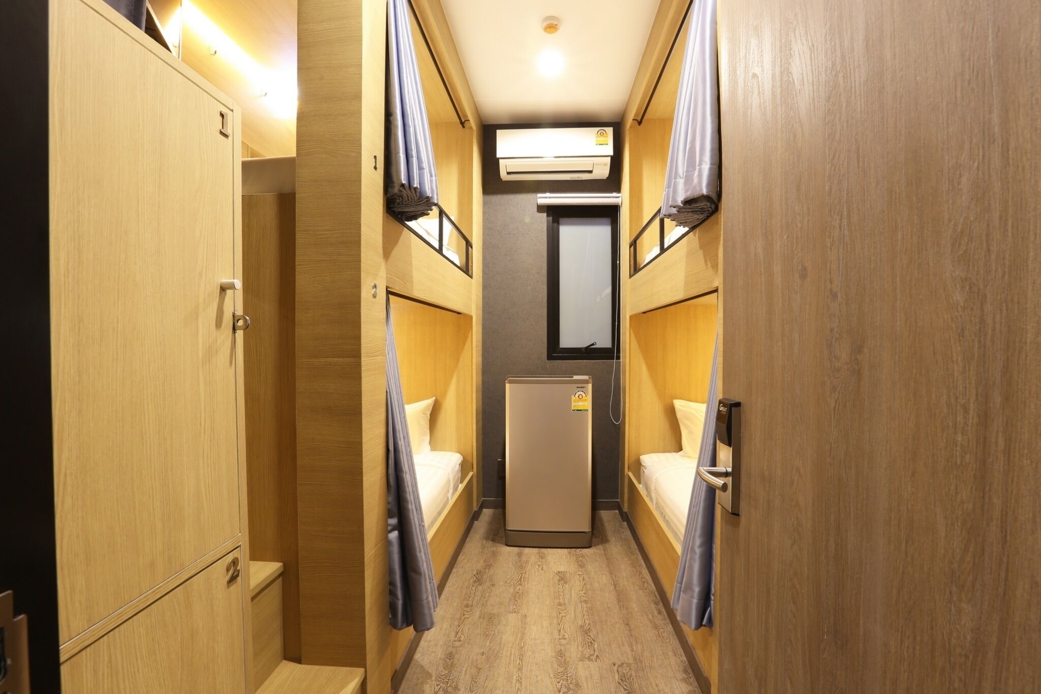 A narrow hallway with bunk beds on either side, a small refrigerator, and a ceiling-mounted air conditioning unit.