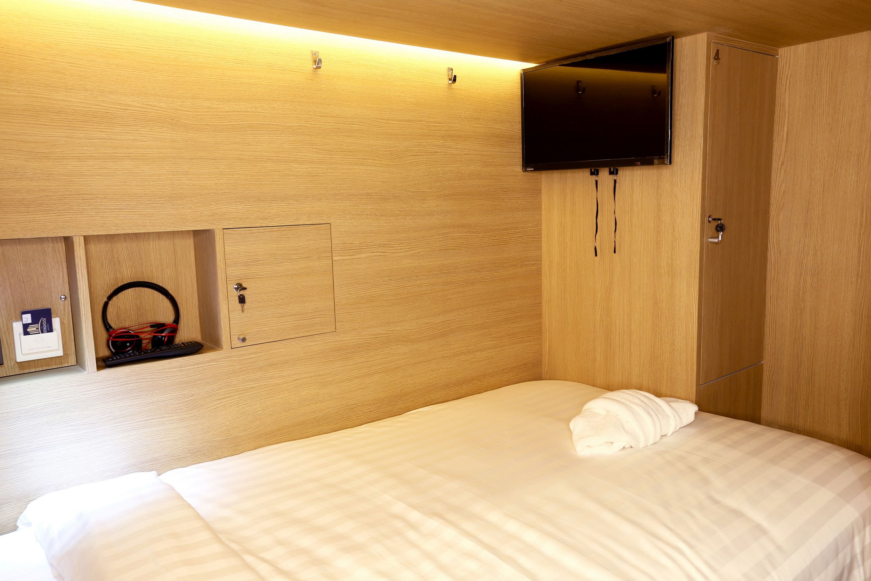 A hotel room with a bed, a television mounted on the wall, and a wardrobe.