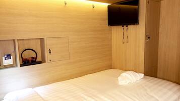 A hotel room with a bed, a television mounted on the wall, and a wardrobe.