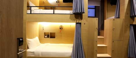 A hotel room with a bunk bed, a desk with a chair, a TV mounted on the wall, and a wardrobe with a mirror.