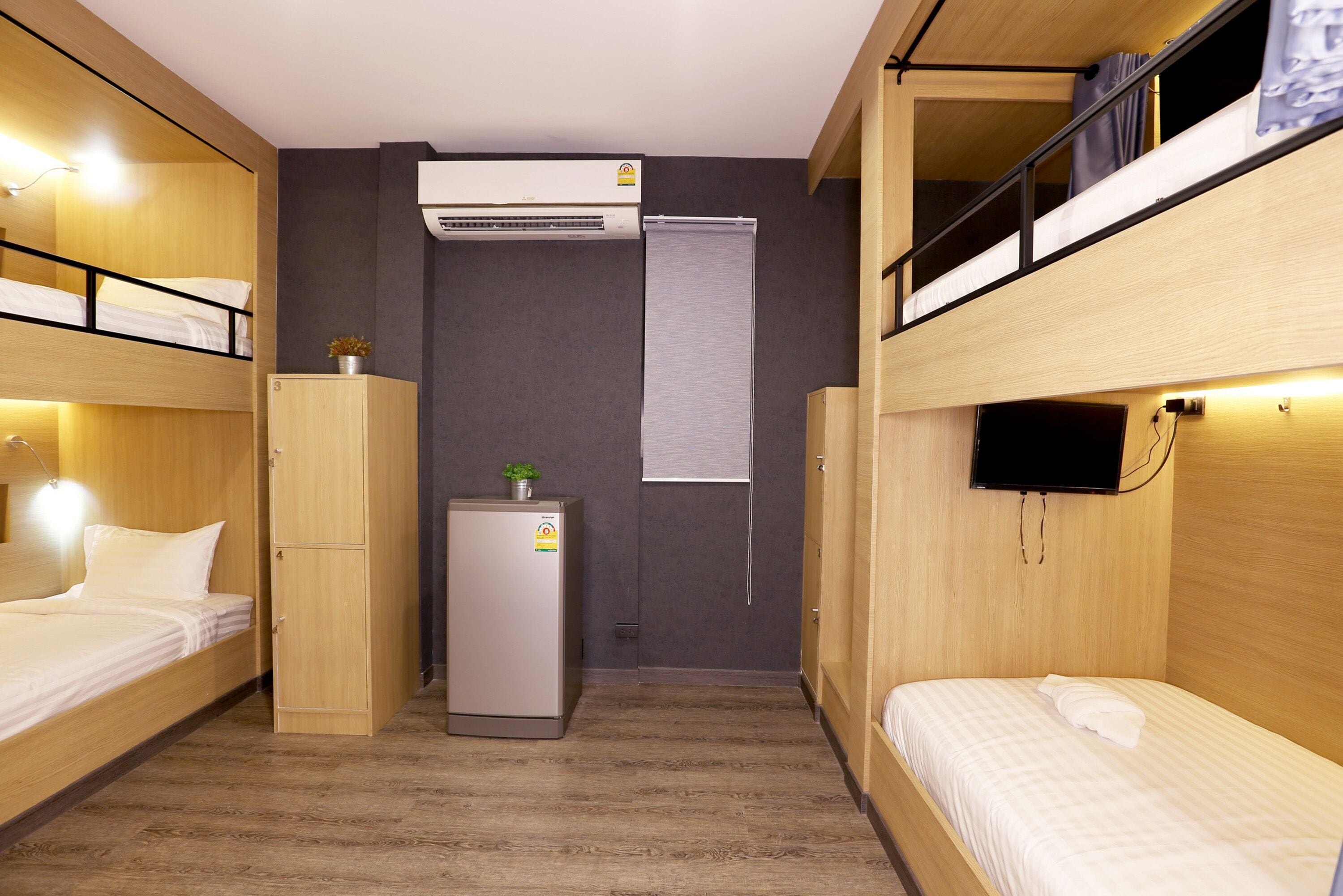 A compact hotel room with bunk beds, a small refrigerator, an air conditioner, and a television.