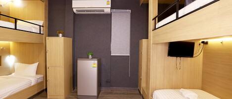 A compact hotel room with bunk beds, a small refrigerator, an air conditioner, and a television.