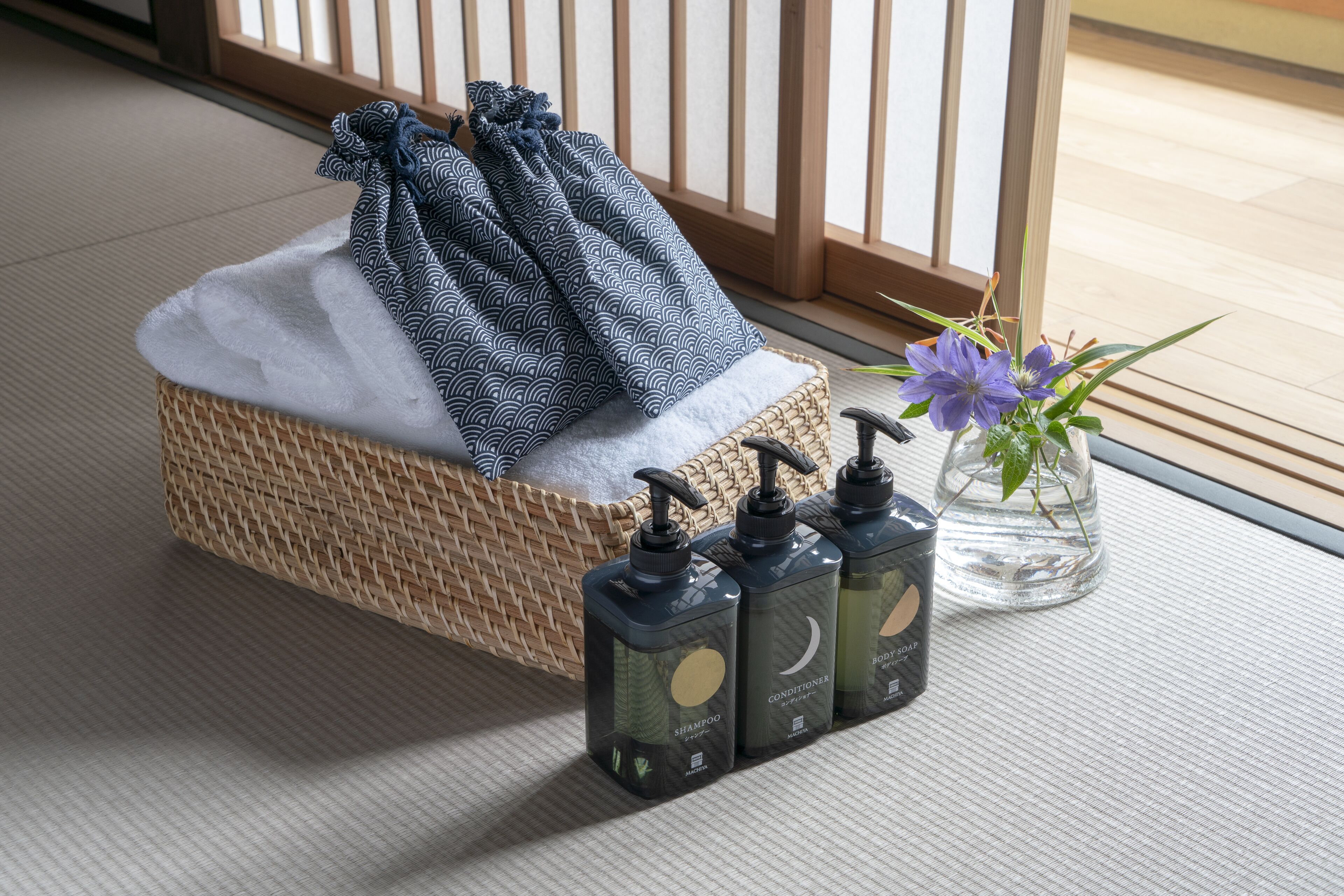 Quarto com cesta de tecido contendo uma toalha, pequeno vaso com planta e três frascos de shampoo e condicionador.