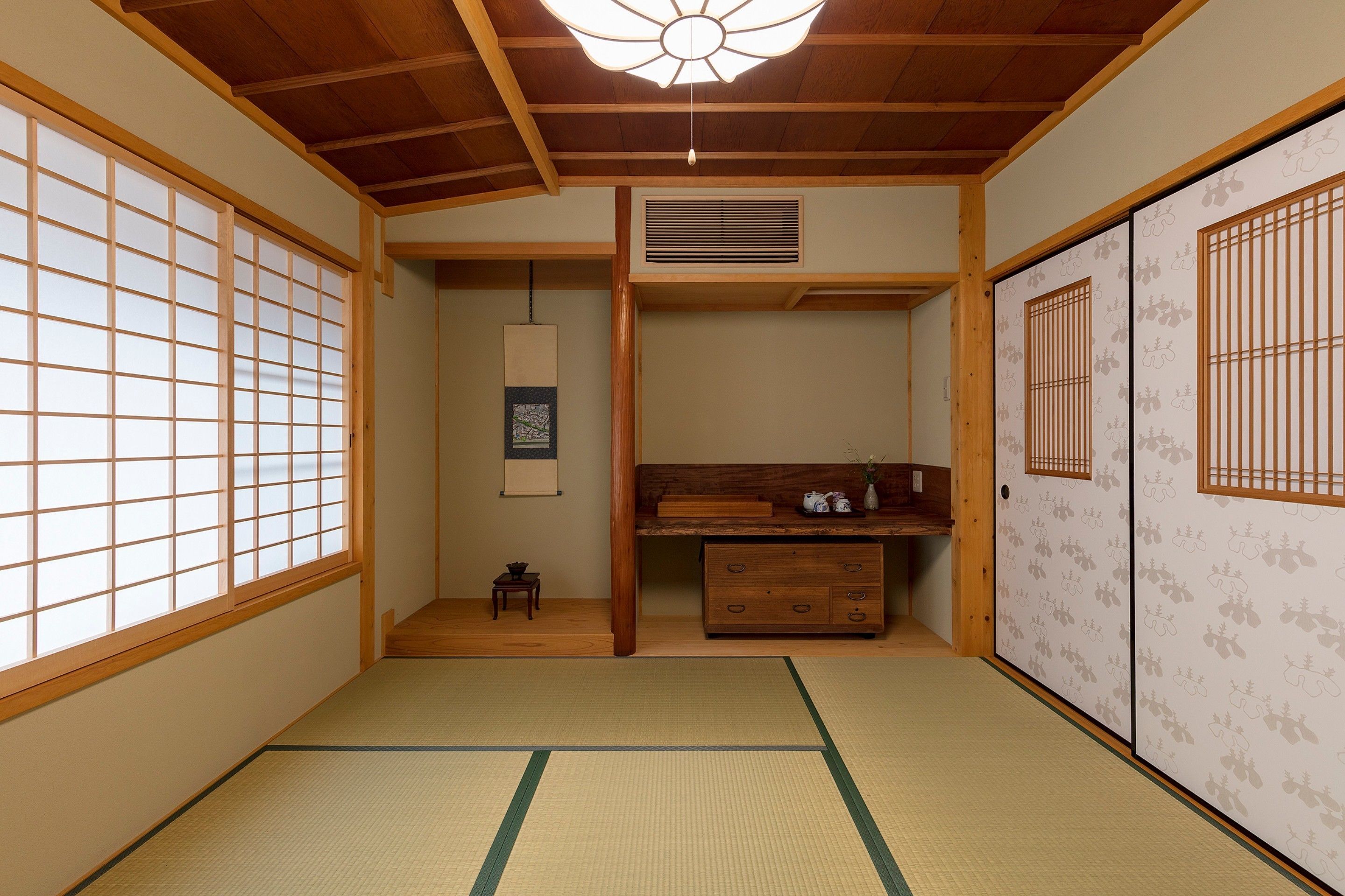 Una habitación japonesa tradicional con suelo de tatami, puertas correderas, un escritorio de madera y una lámpara colgante.