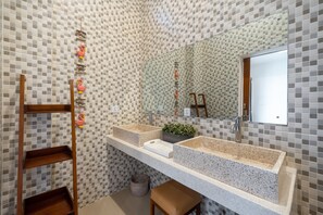 A bathroom with a tiled backsplash, two sinks, a mirror, a wooden ladder, and a small plant.