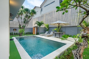 A modern outdoor pool area with a wooden fence, lounge chairs, and a tree.