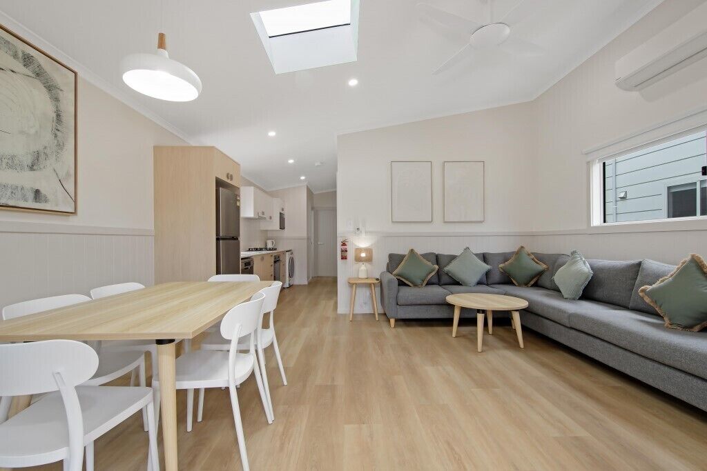 Un salon moderne avec une table à manger, des chaises blanches, un canapé gris et une petite table ronde.