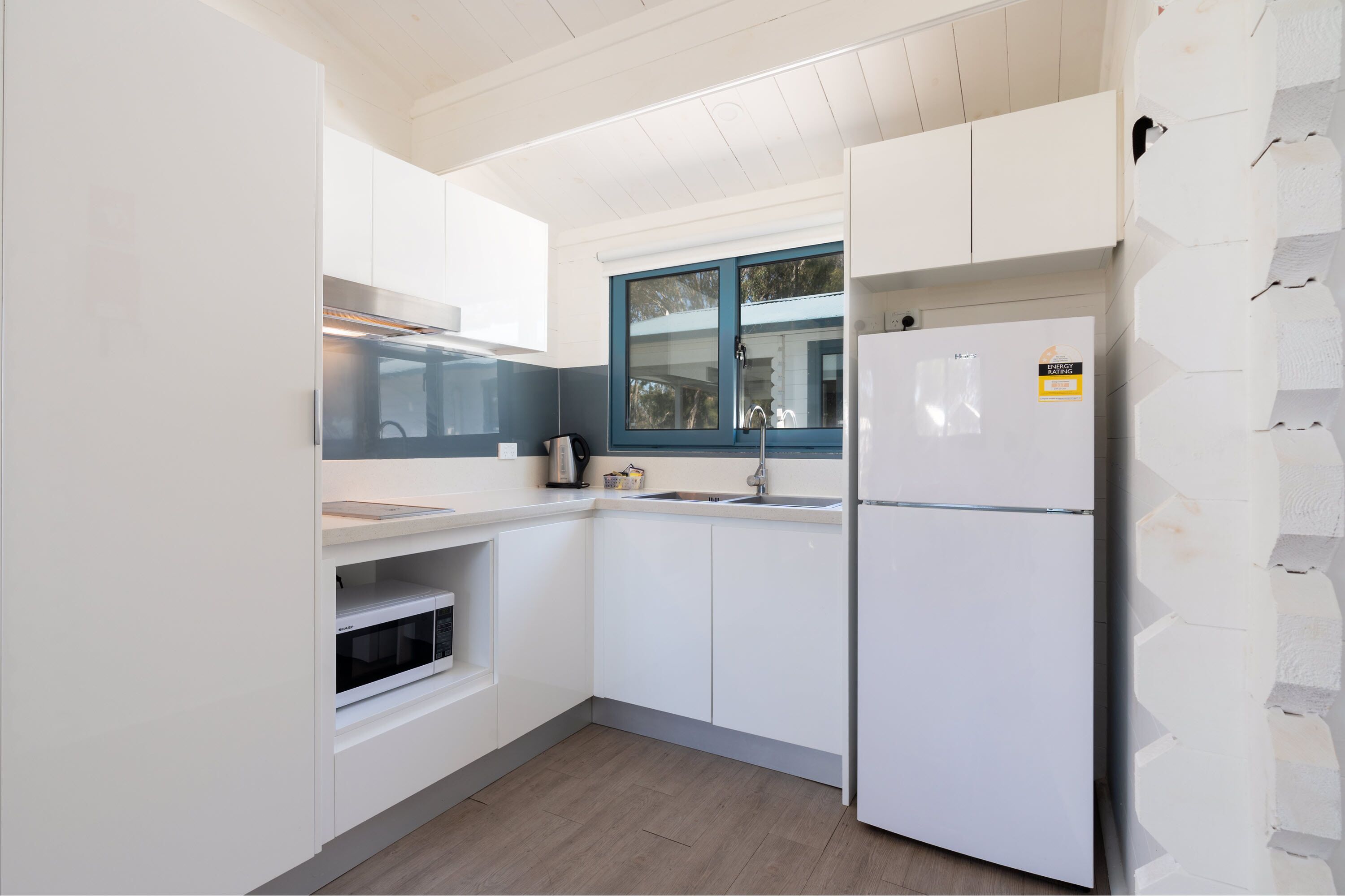 A compact kitchen with white cabinets, a built-in oven, a refrigerator, and a window with blue framing.