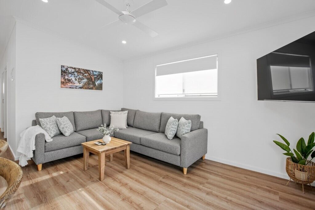 Een moderne woonkamer met een grijze bank, een houten salontafel, een witte muur en een plafondventilator.