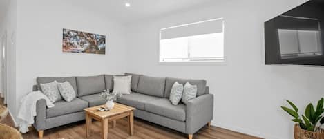 A modern living room with a grey sofa, a wooden coffee table, a white wall, and a ceiling fan.