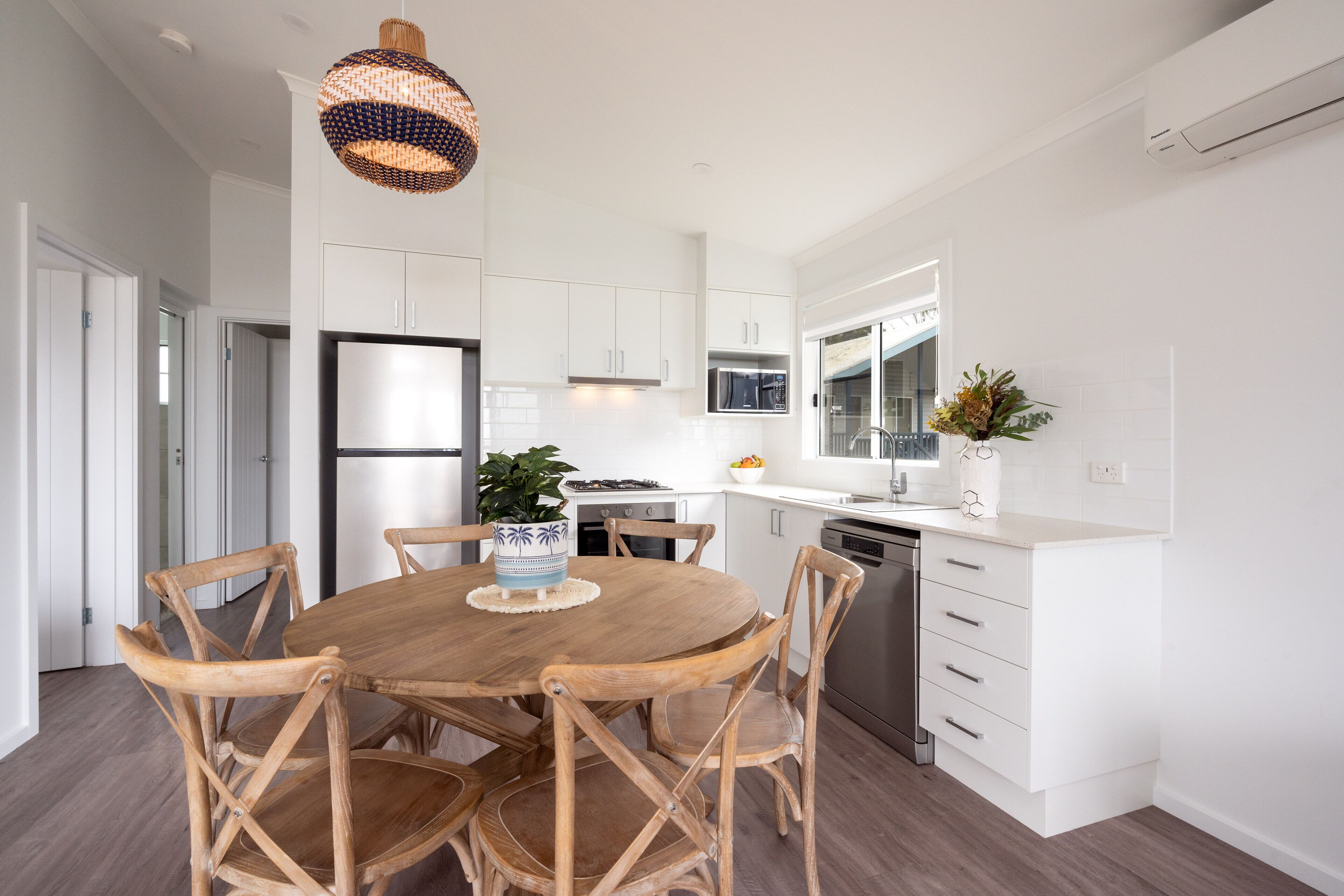 Una cocina moderna con armarios blancos, una mesa de comedor de madera con seis sillas y una lámpara colgante.