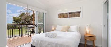 Un dormitorio con una cama grande, una mesita, una silla y un balcón con vistas al exterior.