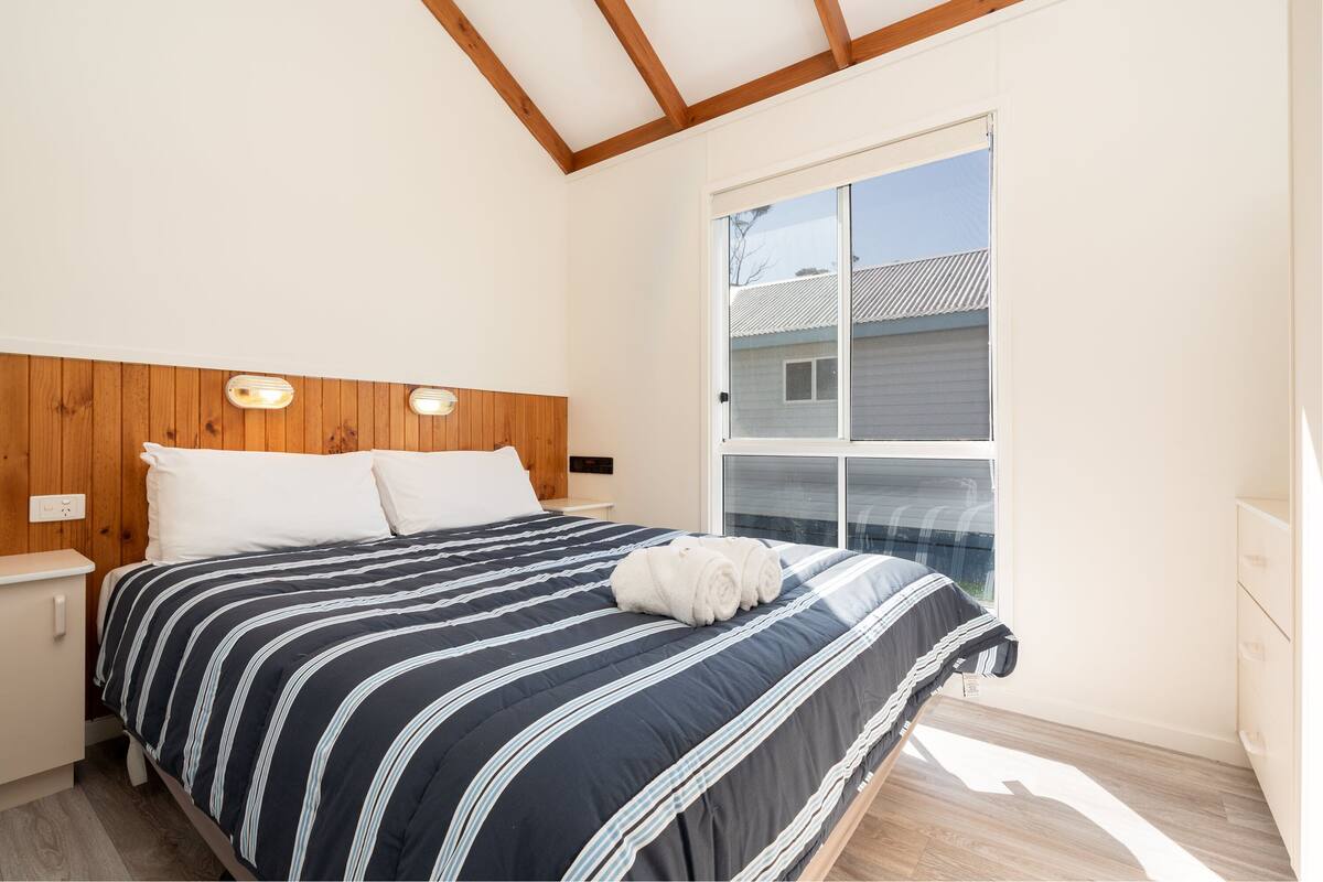 A bedroom with a bed, wooden headboard, bedside tables, and a large window.