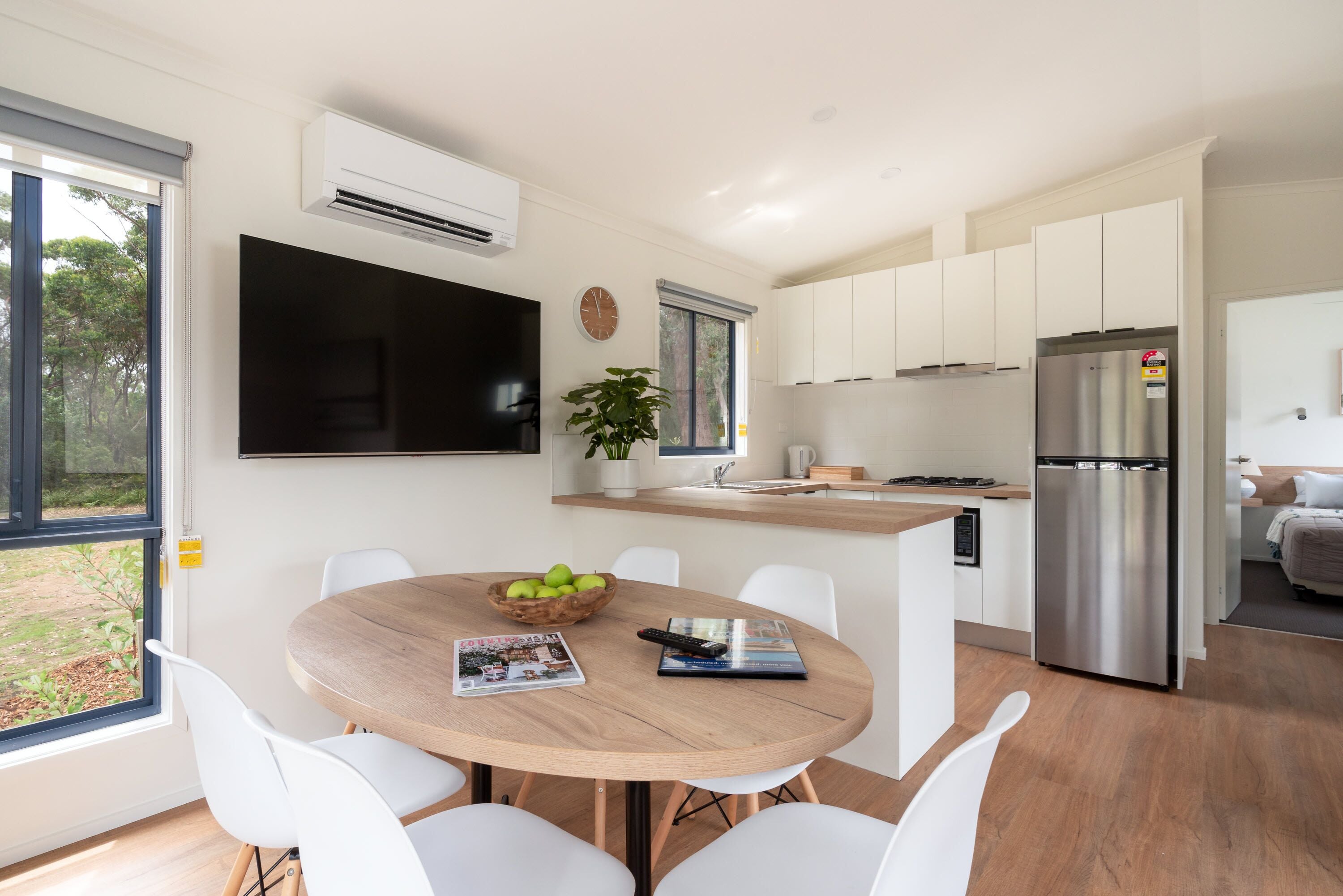 A modern kitchen with white cabinets, a stainless steel refrigerator, and a dining area with a wooden table and white chairs.