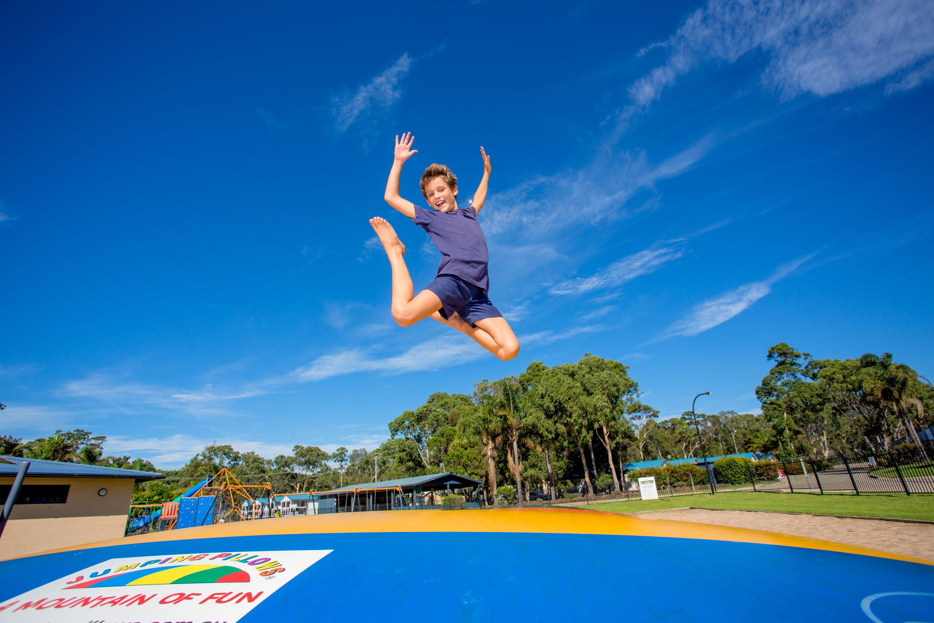A trampoline park with a clear blue sky and trees in the background.