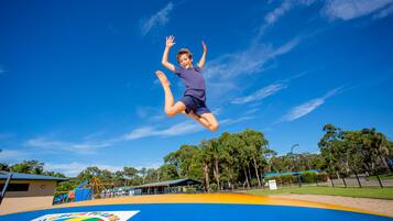 A trampoline park with a clear blue sky and trees in the background.