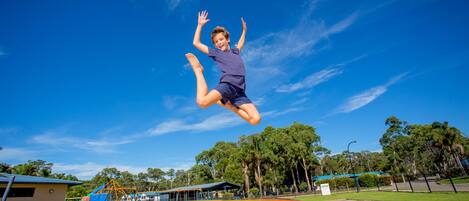 A trampoline park with a clear blue sky and trees in the background.