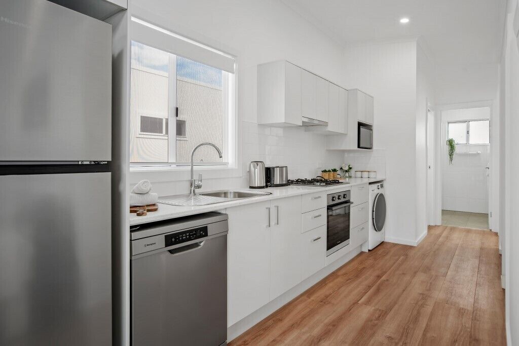 A modern kitchen with white cabinets, stainless steel appliances, a dishwasher, and a washing machine.